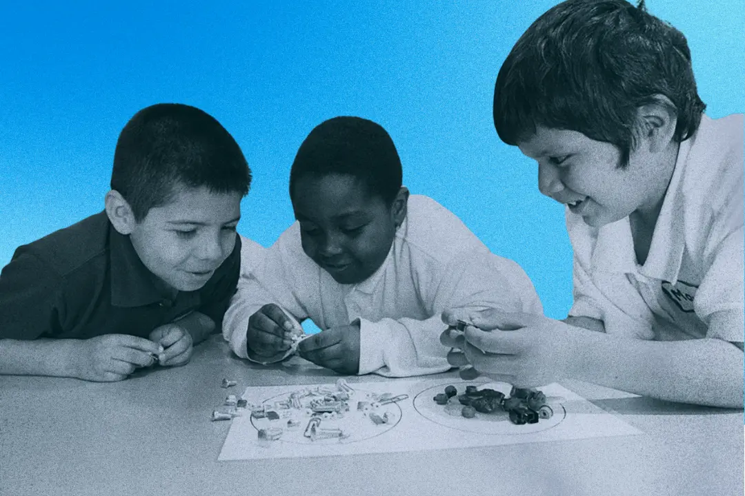 Three children collaborate on a STEM activity at a classroom table, organizing bolts, screws, and small objects for a group project